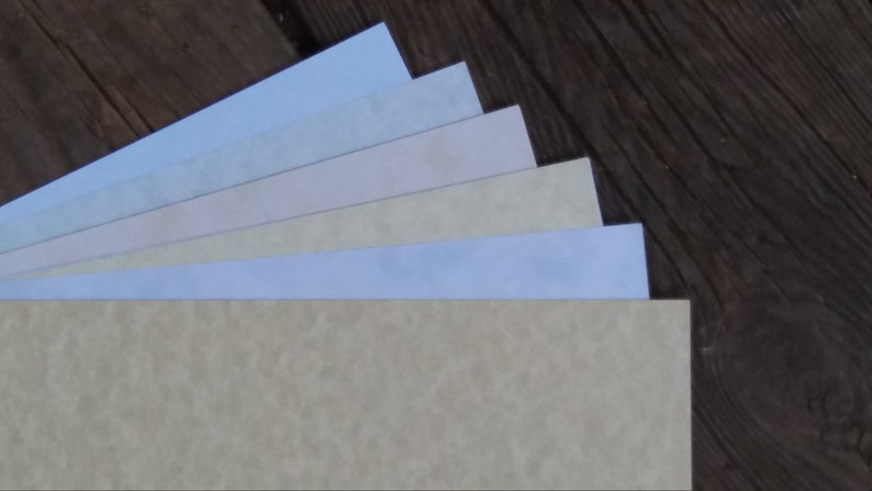 Puede incluir: Una pila de seis hojas de papel de diferentes colores, que van del azul claro al beige, con una superficie texturizada. El papel est&aacute; dispuesto en forma de abanico, con el color m&aacute;s claro en la parte superior y el color m&aacute;s oscuro en la parte inferior.