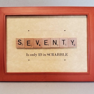 May include: A framed artwork with the word "SEVENTY" spelled out using Scrabble tiles. The text "Is only 13 in SCRABBLE" is below the tiles. The frame is a reddish-orange color.