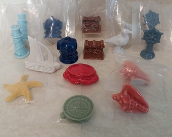 May include: A collection of 13 miniature ceramic figurines with nautical themes. The figurines include a lighthouse, sailboat, diving helmet, treasure chest, seagull, ship's wheel, starfish, compass, and seashells.