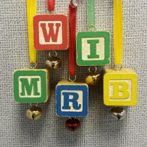May include: Five wooden blocks with letters spelling out "W I M R B" hanging from yellow, red, and green ribbon with bells attached to each block.