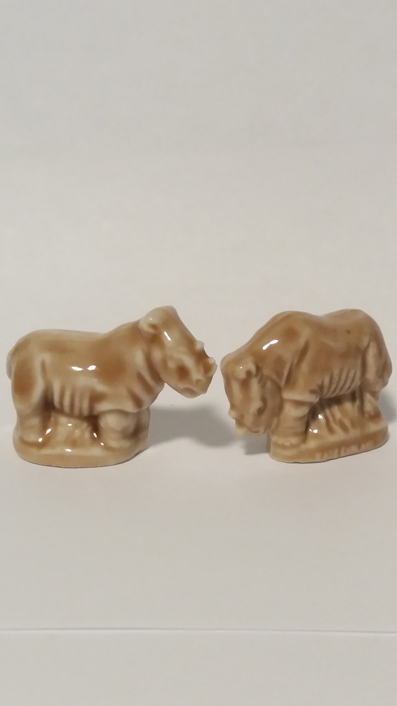 Może przedstawiać: Dwie brązowe ceramiczne figurki nosorożc&oacute;w, kt&oacute;re patrzą na siebie.
