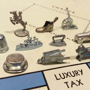 May include: A collection of ten silver Monopoly game pieces, including a thimble, a battleship, a top hat, a shoe, a wheelbarrow, an iron, a race car, a dog, a horse, and a cannon.