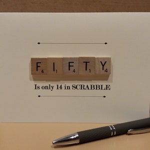 May include: A white card with the word "FIFTY" spelled out using Scrabble tiles. The tiles are arranged in a row and the point values are visible on each tile. The text "Is only 14 in SCRABBLE" is printed below the tiles.
