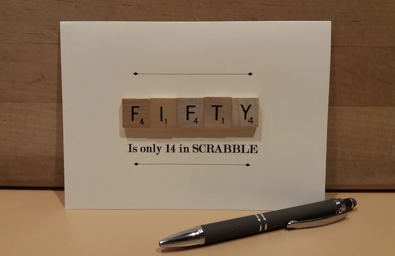 May include: A white card with the word "FIFTY" spelled out using Scrabble tiles. The tiles are arranged in a row and the point values are visible on each tile. The text "Is only 14 in SCRABBLE" is printed below the tiles.