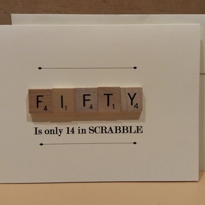 May include: A white card with the word "FIFTY" spelled out using Scrabble tiles. The tiles are arranged in a row and the points for each letter are visible. The text "Is only 14 in SCRABBLE" is printed below the tiles.