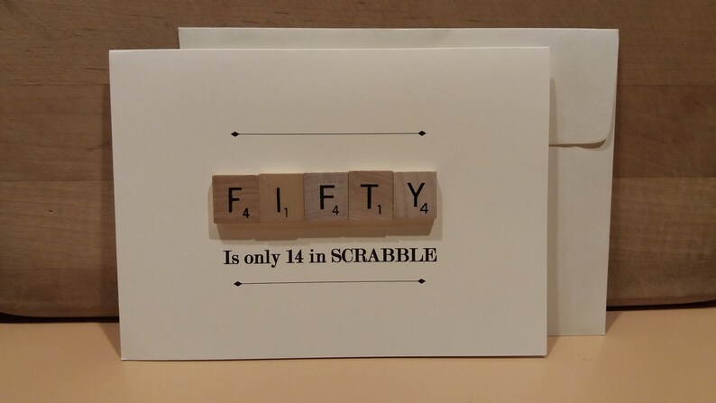 May include: A white card with the word "FIFTY" spelled out using Scrabble tiles. The tiles are arranged in a row and the points for each letter are visible. The text "Is only 14 in SCRABBLE" is printed below the tiles.