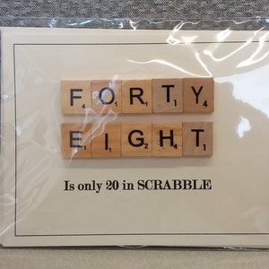 May include: A white card with the word "FORTY-EIGHT" spelled out using Scrabble tiles. The text below the tiles reads "Is only 20 in SCRABBLE".