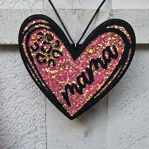May include: A black heart-shaped ornament with pink glitter and the words "So much love, Mama" written in black.