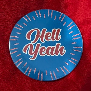 May include: A blue and red round ceramic plate with a white sunburst design and the text "Hell Yeah" in red.