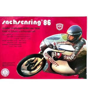 May include: A vintage poster with a red background features a motorcycle racer in a helmet and racing suit. The poster includes the text "sachsenring '86" and "Großer Preis des ADMV der DDR". The motorcycle is white and black with the word "SPORETT" on the side.