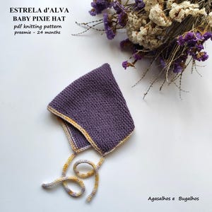 Könnte beinhalten: Ein gestrickter, violetter Baby-Pixie-Hut mit gelben und weißen Verzierungen und Bindebändern. Der Hut ist handgefertigt und trägt den Text "ESTRELA D'ALVA BABY PIXIE HAT pdf knitting pattern preemie - 24 months".