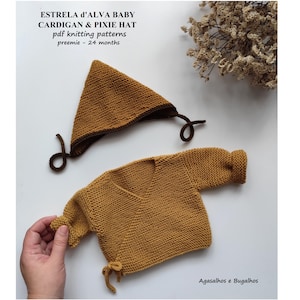 Può includere: Un set per neonati lavorato a maglia color giallo senape e marrone, composto da un cardigan e un cappello a punta. Il cappello è triangolare con bordi e lacci marroni scuri. Il cardigan ha maniche lunghe e scollo a V. Il testo recita "ESTRELA d'ALVA BABY CARDIGAN & PIXIE HAT".