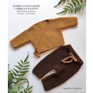 May include: Mustard yellow knitted baby cardigan and brown knitted trousers set. The cardigan has a wrap-style design with tie closures. The trousers have a drawstring waist. The text "ESTRELA D'ALVA BABY CARDIGAN & PANTS" is visible.