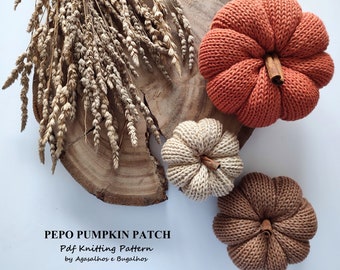 May include: Three knitted pumpkins in orange, beige, and brown on a wooden surface. The pumpkins are decorated with cinnamon sticks. The text "PEPO PUMPKIN PATCH Pdf Knitting Pattern by Agasalhos e Bugalhos" is visible at the bottom of the image.