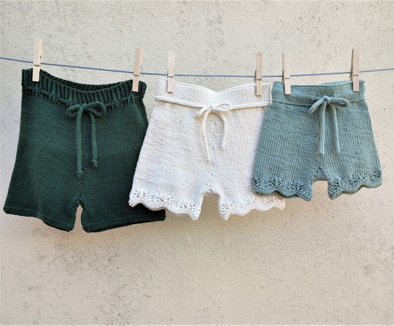 May include: Three pairs of knitted shorts hanging on a clothesline. The shorts are green, white, and light blue. The shorts have a scalloped edge.