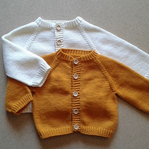 May include: Two knitted baby cardigans, one white and one mustard yellow, with wooden buttons.