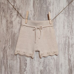 May include: A pair of cream-colored knitted shorts with a lace trim and a drawstring tie.