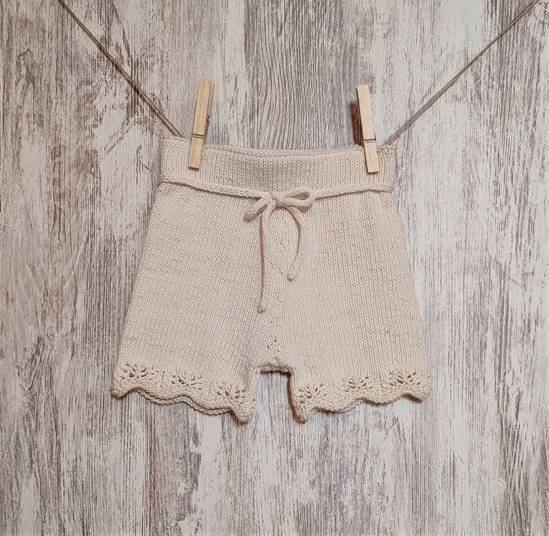 May include: A pair of cream-colored knitted shorts with a lace trim and a drawstring tie.