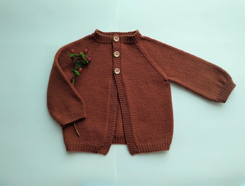 May include: A brown knitted cardigan with wooden buttons. The cardigan has a round neckline and long sleeves.