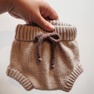 May include: Beige knitted baby bloomers with a brown drawstring tie.