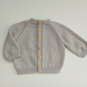 May include: A light gray knitted cardigan with a button closure and wooden buttons.
