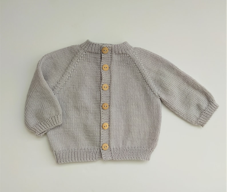 May include: A light gray knitted cardigan with a button closure and wooden buttons.