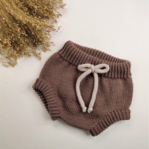 May include: Brown knitted baby bloomers with a white drawstring tie.