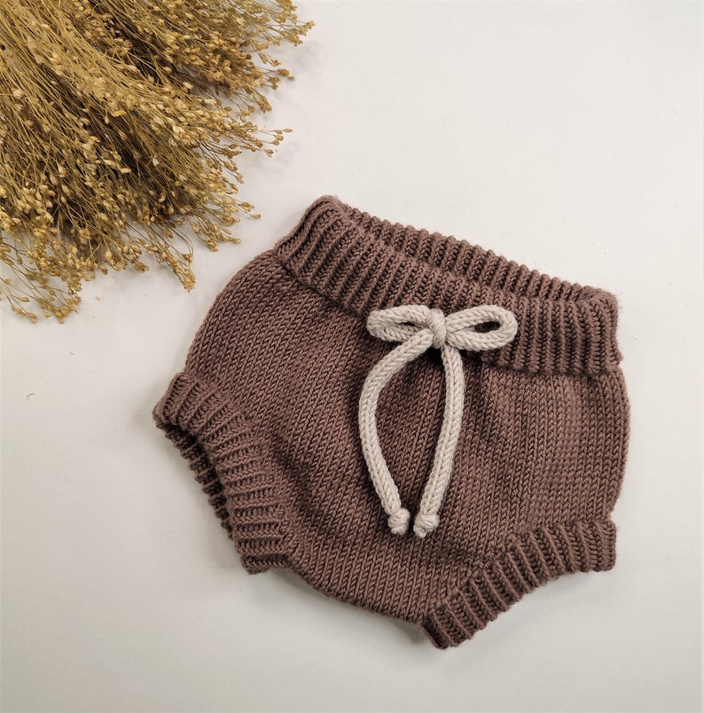 May include: Brown knitted baby bloomers with a white drawstring tie.