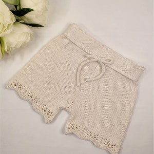 May include: Cream-colored knitted shorts with a lace trim and a drawstring waist.