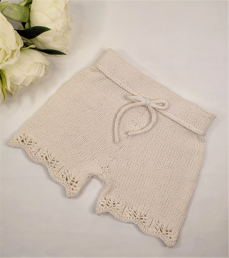 May include: Cream-colored knitted shorts with a lace trim and a drawstring waist.