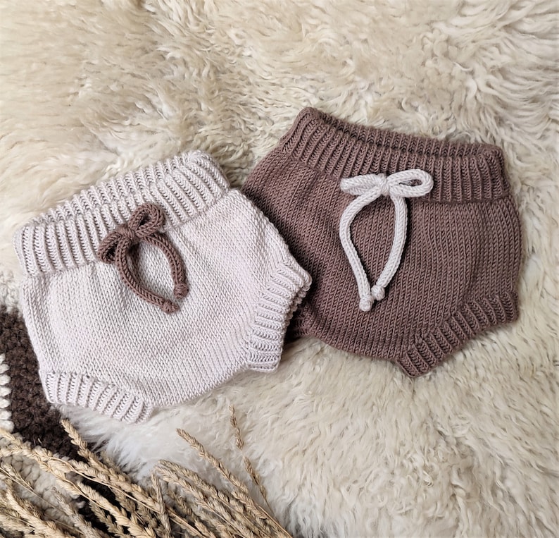 May include: Two pairs of knitted baby bloomers. One pair is beige with brown ties and the other pair is brown with white ties.