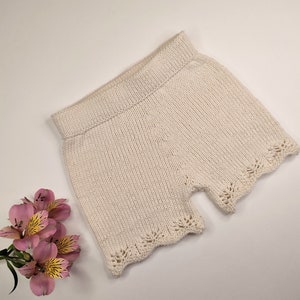 May include: A pair of cream-colored knitted shorts with a delicate lace trim around the edges.