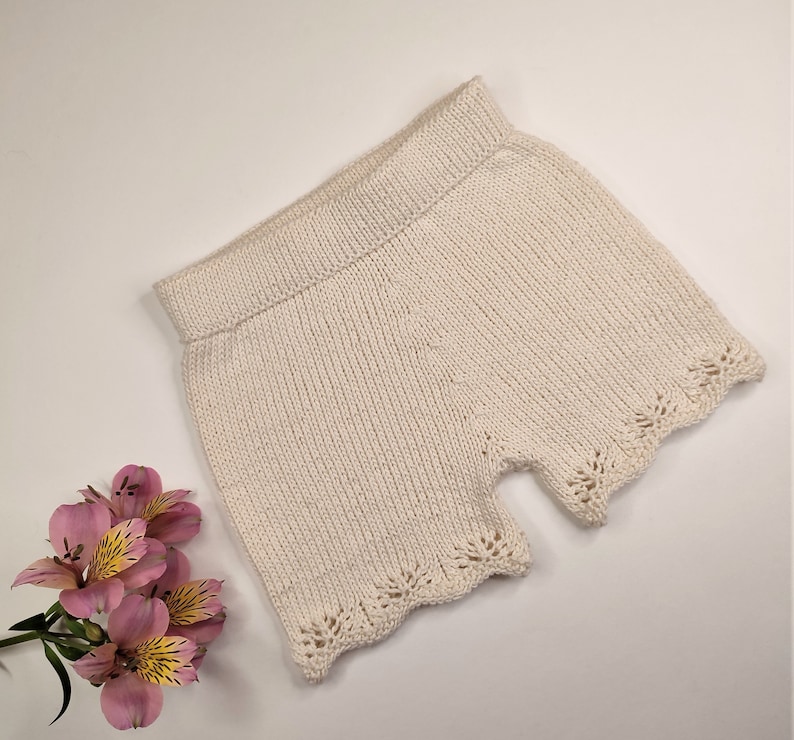 May include: A pair of cream-colored knitted shorts with a delicate lace trim around the edges.