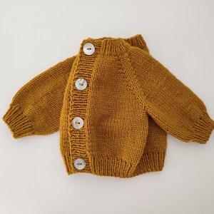 May include: A mustard yellow knitted cardigan with four white buttons down the front.