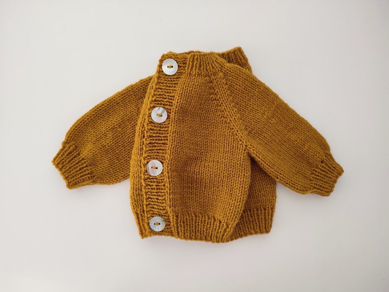 May include: A mustard yellow knitted cardigan with four white buttons down the front.
