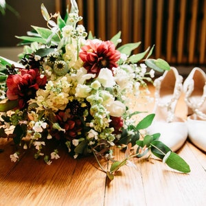 May include: A bridal bouquet with white, red, and green flowers, and a pair of white satin shoes.