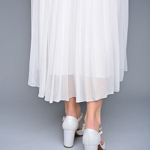 May include: White pleated skirt with white heeled shoes featuring a jeweled buckle.