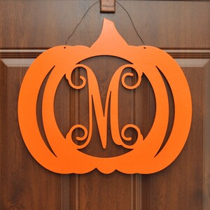 May include: Orange wooden pumpkin door hanger with a cutout of the letter "M" in the center.