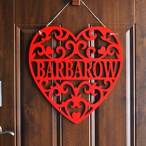 May include: Red wooden heart-shaped door hanger with a decorative design and the name "BARBAROW" cut out in the center.