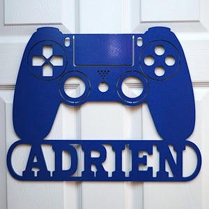 May include: A blue metal cutout of a video game controller with the name "ADREN" underneath.