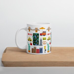 May include: White ceramic mug featuring colorful illustrations of New York City landmarks and icons, including the Brooklyn Bridge, Statue of Liberty, yellow taxi cabs, and a hot dog cart. The mug has the text "I NYC".