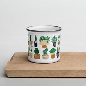 May include: White enamel mug with a pattern of green potted succulents and cacti. The mug has a silver rim.
