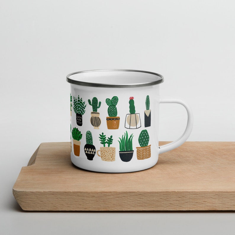 May include: White enamel mug with a pattern of green potted cacti and succulents. The mug has a silver rim and a black handle.