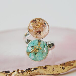 May include: A silver ring with two round resin inlays. The top inlay is peach with gold flecks. The bottom inlay is turquoise with gold flecks.