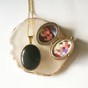 Puede incluir: Un collar de cadena dorada con un colgante de medallón ovalado negro y un medallón más pequeño con una foto en su interior. Los medallones están sobre una superficie de ágata blanca.