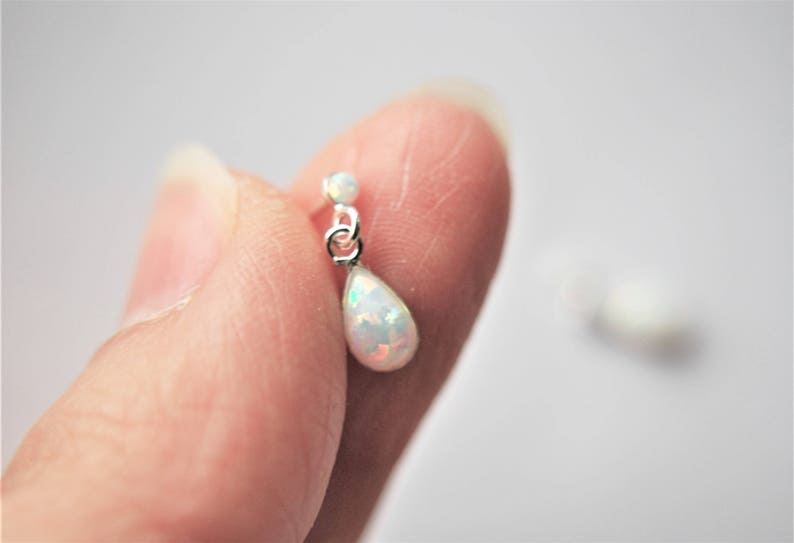 May include: A pair of silver teardrop earrings with a white opal stone.