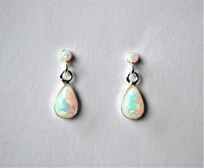 May include: A pair of silver teardrop earrings with white opal stones. The earrings have a small round silver bead at the top and a larger teardrop-shaped opal stone hanging below.