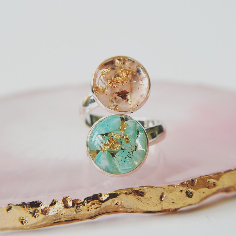 May include: A silver ring with two round resin inlays. The top inlay is peach with gold flecks. The bottom inlay is turquoise with gold flecks.