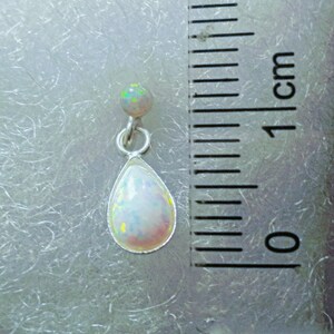 May include: A teardrop-shaped opal pendant earring with a small opal bead at the top. The earring is silver and measures approximately 1 cm in length.
