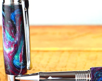 May include: A black and blue pen with silver accents and a swirling pattern. The pen is lying on a wooden surface.